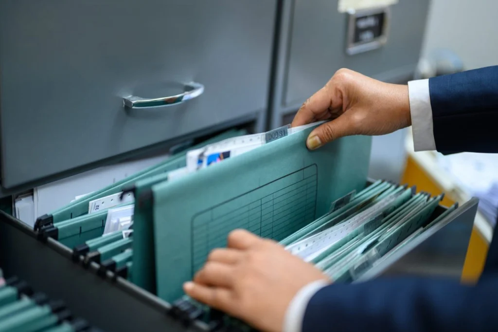 A businessman in formal attire carefully selects a file from a meticulously maintained filing cabinet filled with neatly arranged documents.